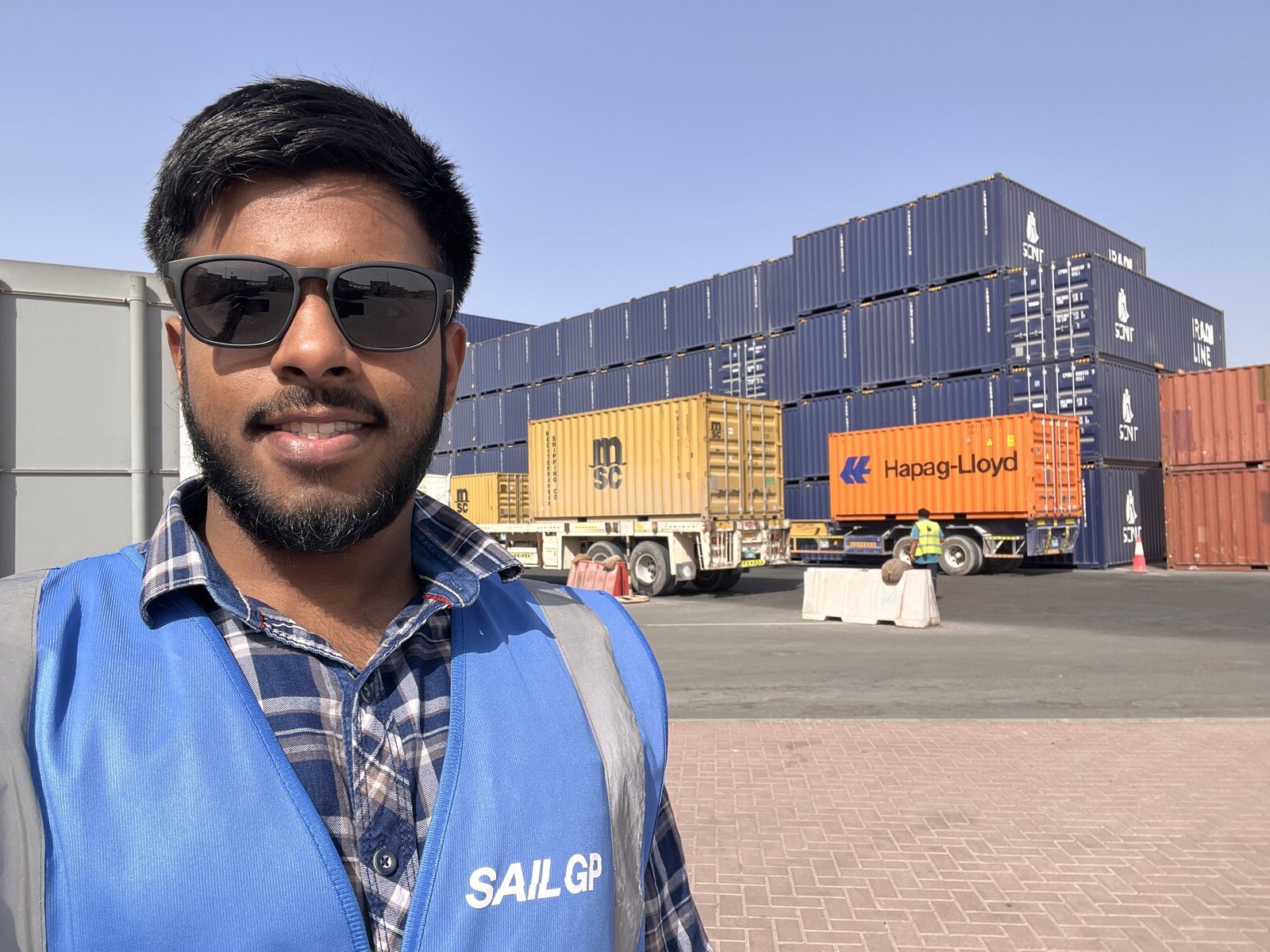 Kenny Colaco in a SailGP vest in front of a stacked container yard with Hapag-Lloyd and MSC boxes